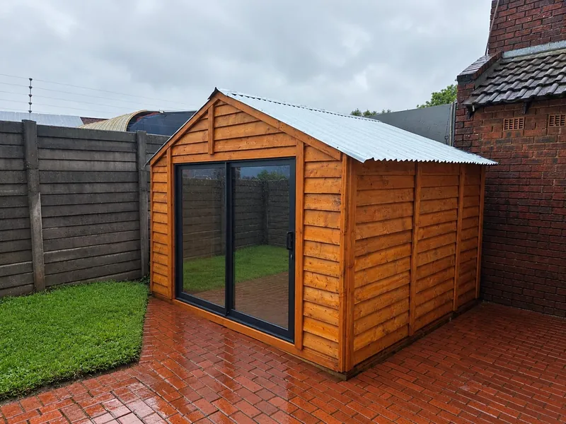 Orange stained wooden garden room with a black sliding door beside paving